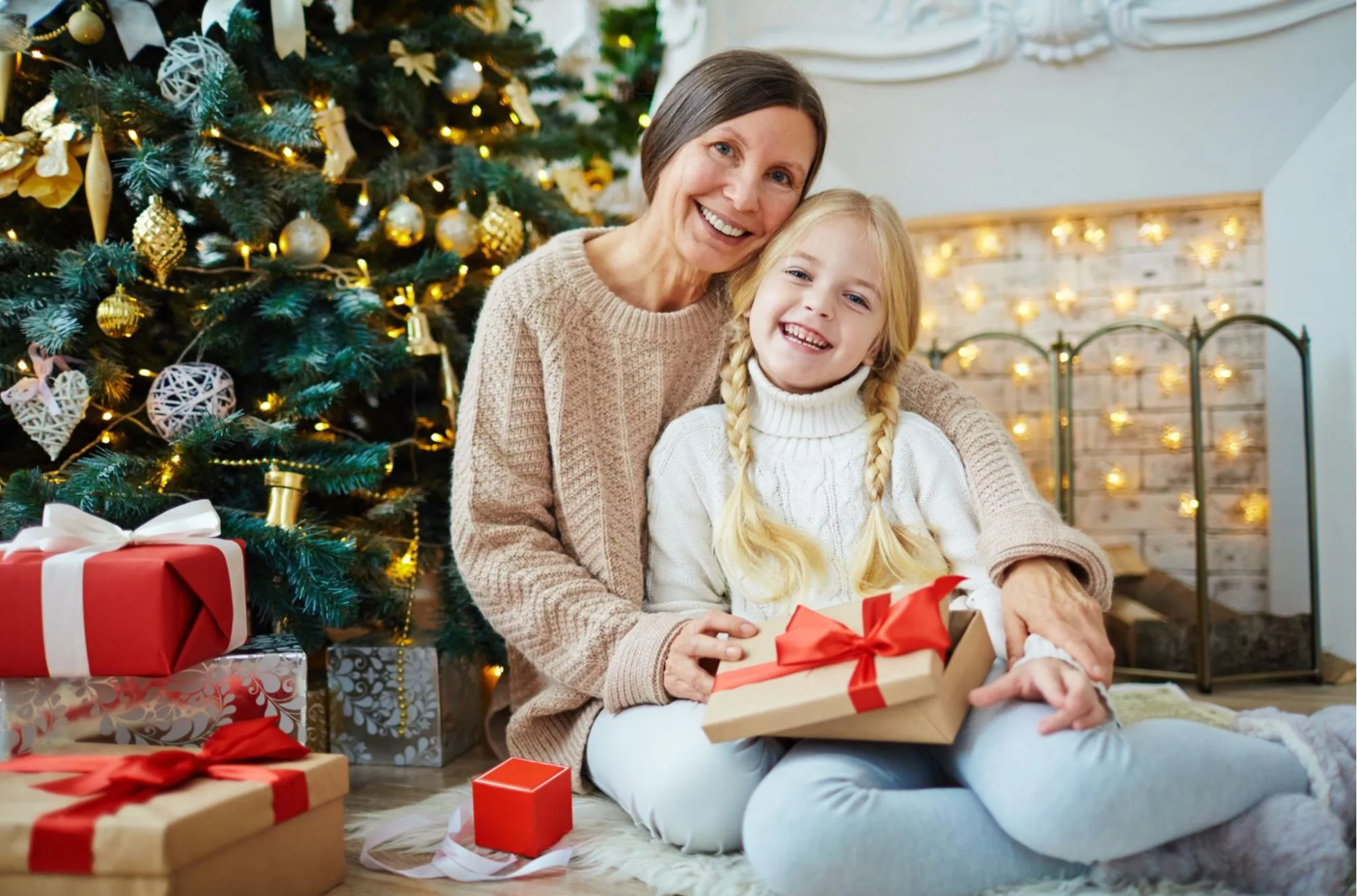 mother and daughter siting by christmas treesmiling 