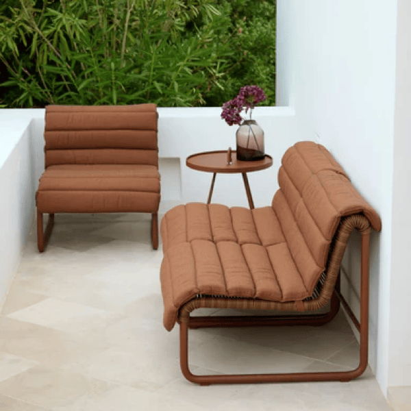 Modern outdoor lounge chairs with cushioned rust-colored upholstery and slim powder-coated aluminum frames on a covered patio.