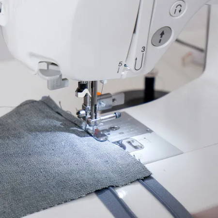 A sewing machine that is sewing a piece of fabric to a zipper using the adjustable zipper foot