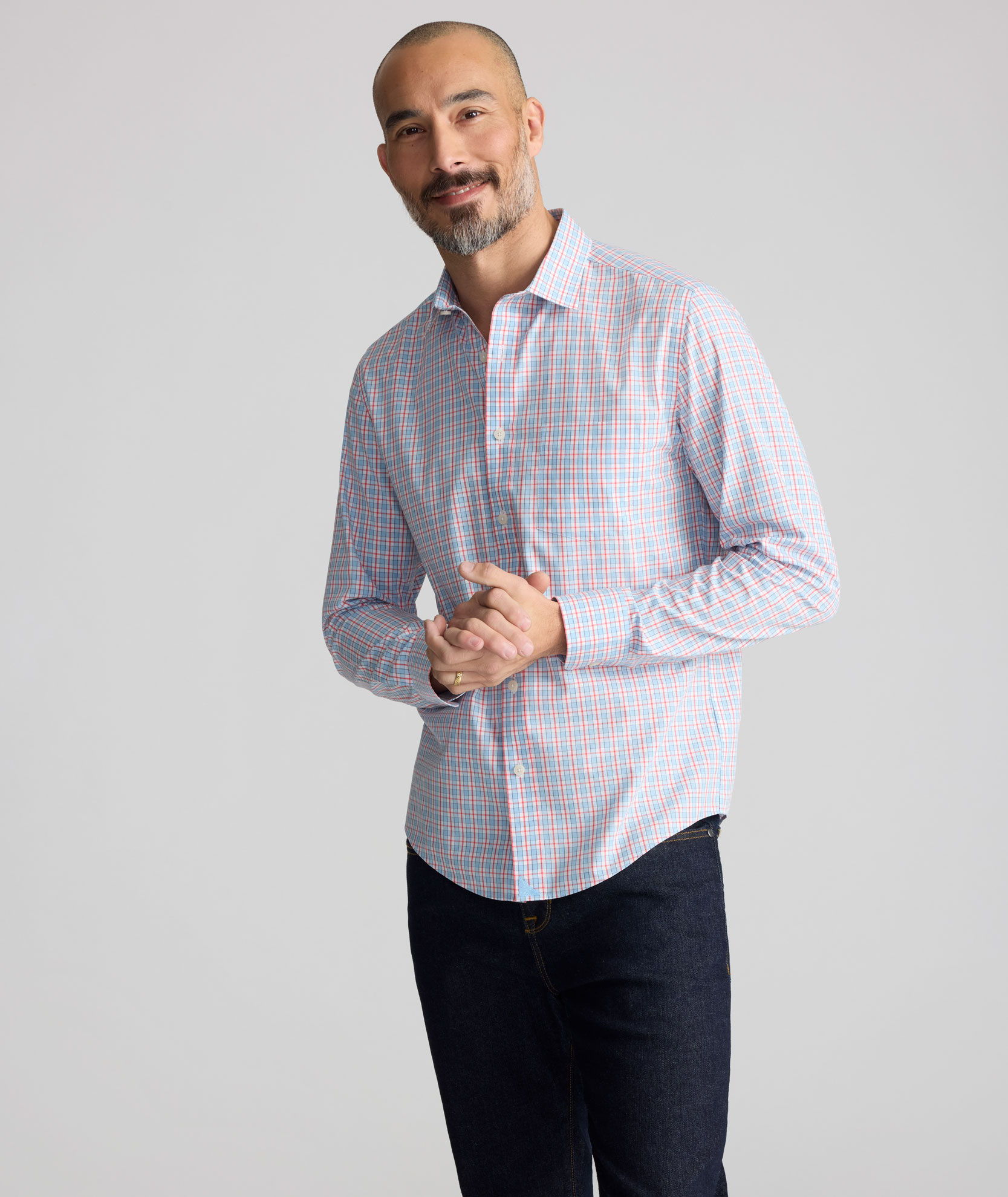 Man in a striped shirt smiling and standing with hands clasped.