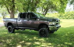 Side profile of lifted gray RAM 2500 Heavy Duty with black wheels and tonneau cover parked on grassy lawn