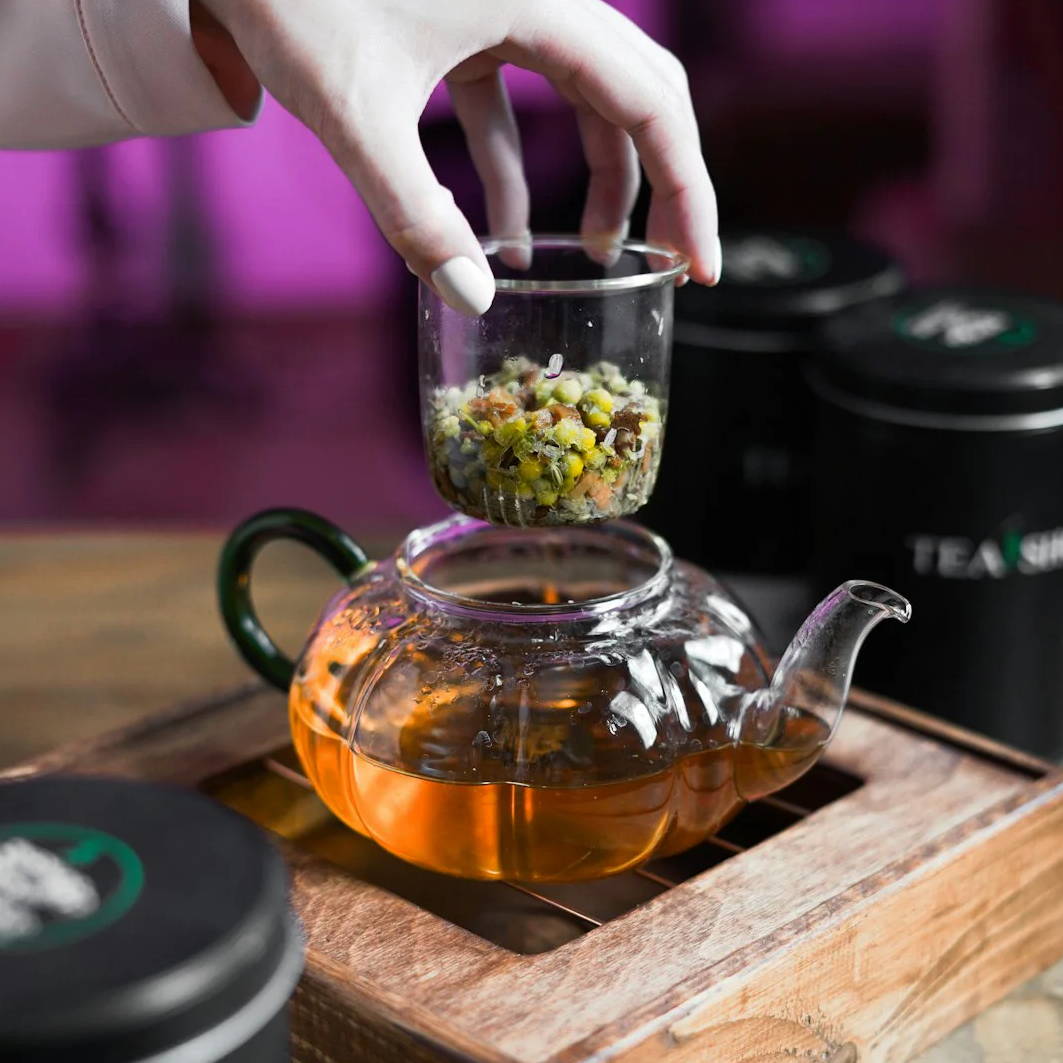 a person is putting food in a glass teapot