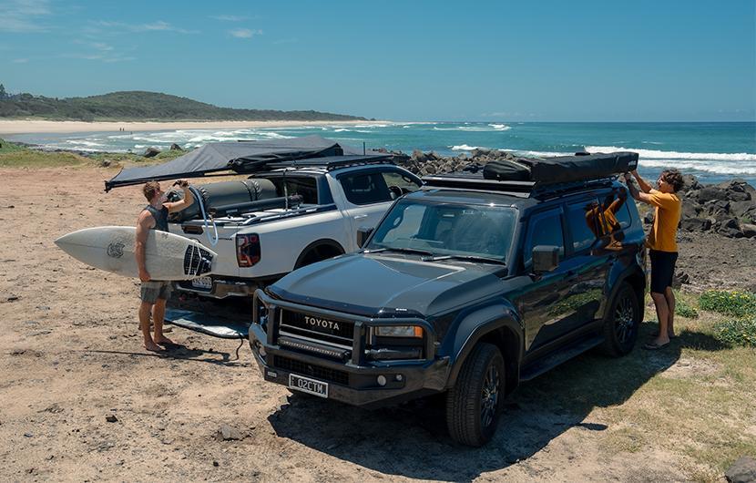 Two Four Wheel Drives near the beach with people unloading gear off the platform 