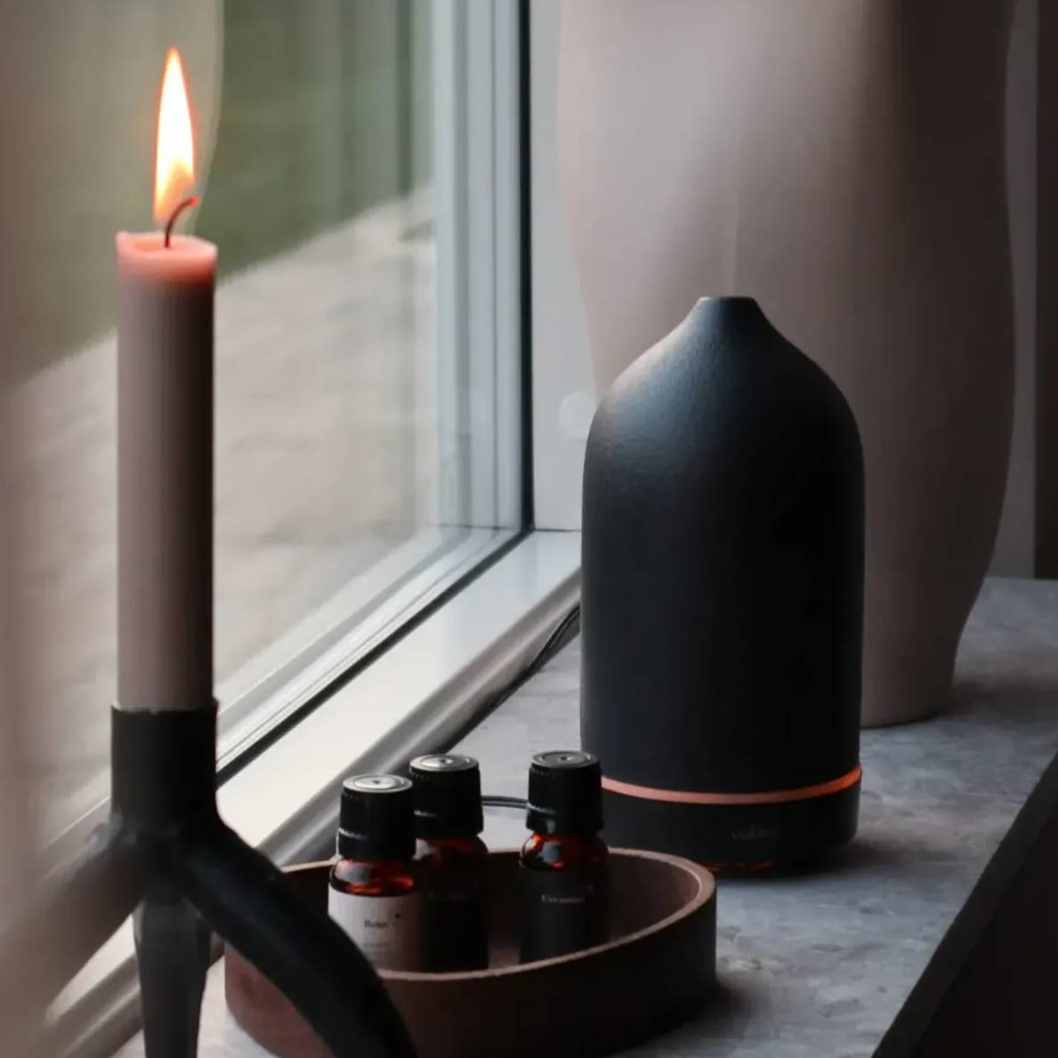 A windowsill with a burning candle and black diffuser. 