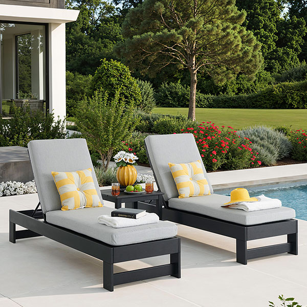 Two lounge chairs by a pool with decorative pillows and a side table.