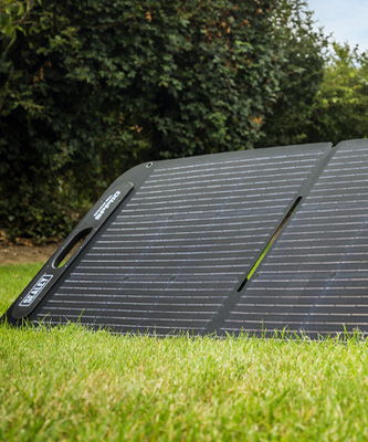 A solar panel resting on green grass in a garden setting.