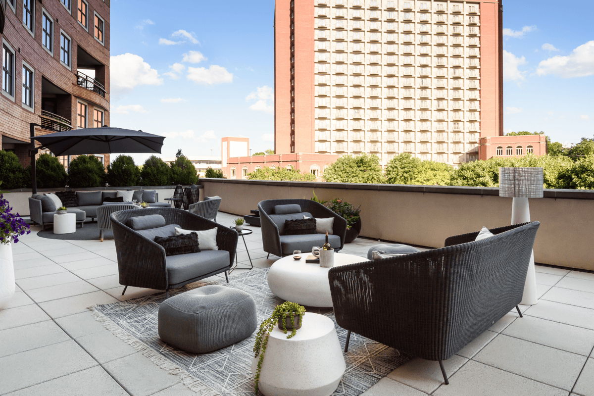 Sophisticated rooftop patio with dark woven outdoor sofas and lounge chairs, concrete side tables, a textured outdoor rug, and a large black umbrella.