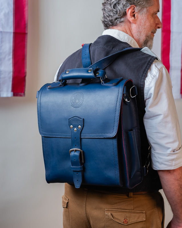 Person wearing a blue backpack, standing in front of flags.