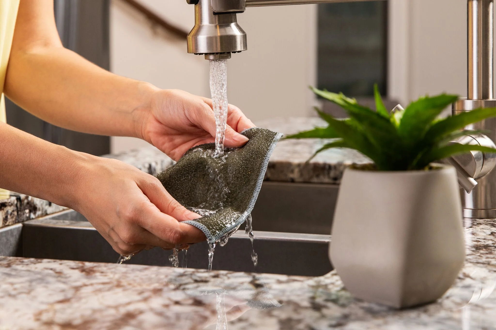Person washing a dish under running water at a kitchen sink.