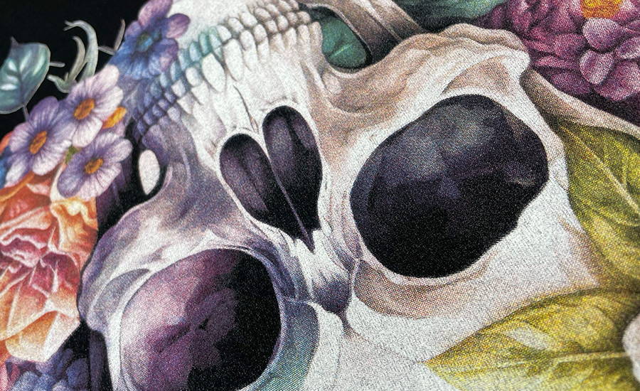 Close up detail of a full colour CMYK screen printed design of a skull surrounded by decorative flowers and leaves. The predominantly white and grey skull is shown cropped and inverted surrounded by sections of flowers and leaves. The artwork has been illustrated in a realism style with detailed shading and gradients creating a dimension and depth.