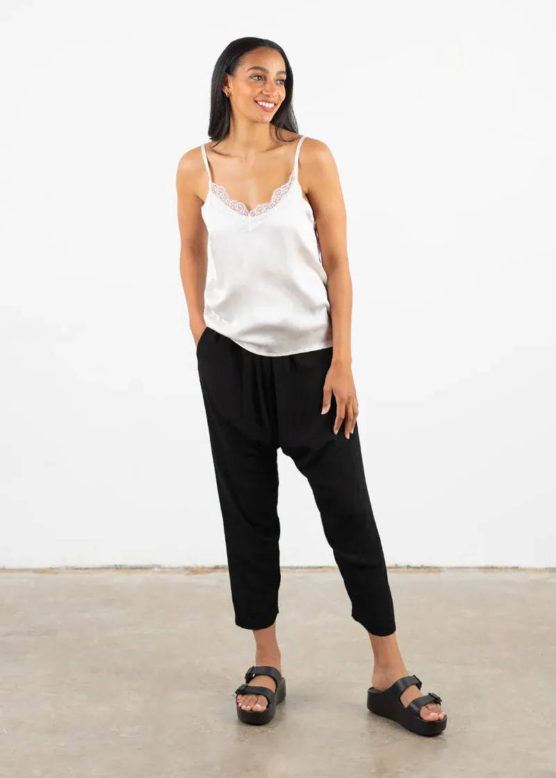A model wearing an off white silky camisole with leacey detail around the neckline with black trousers and black platform slides