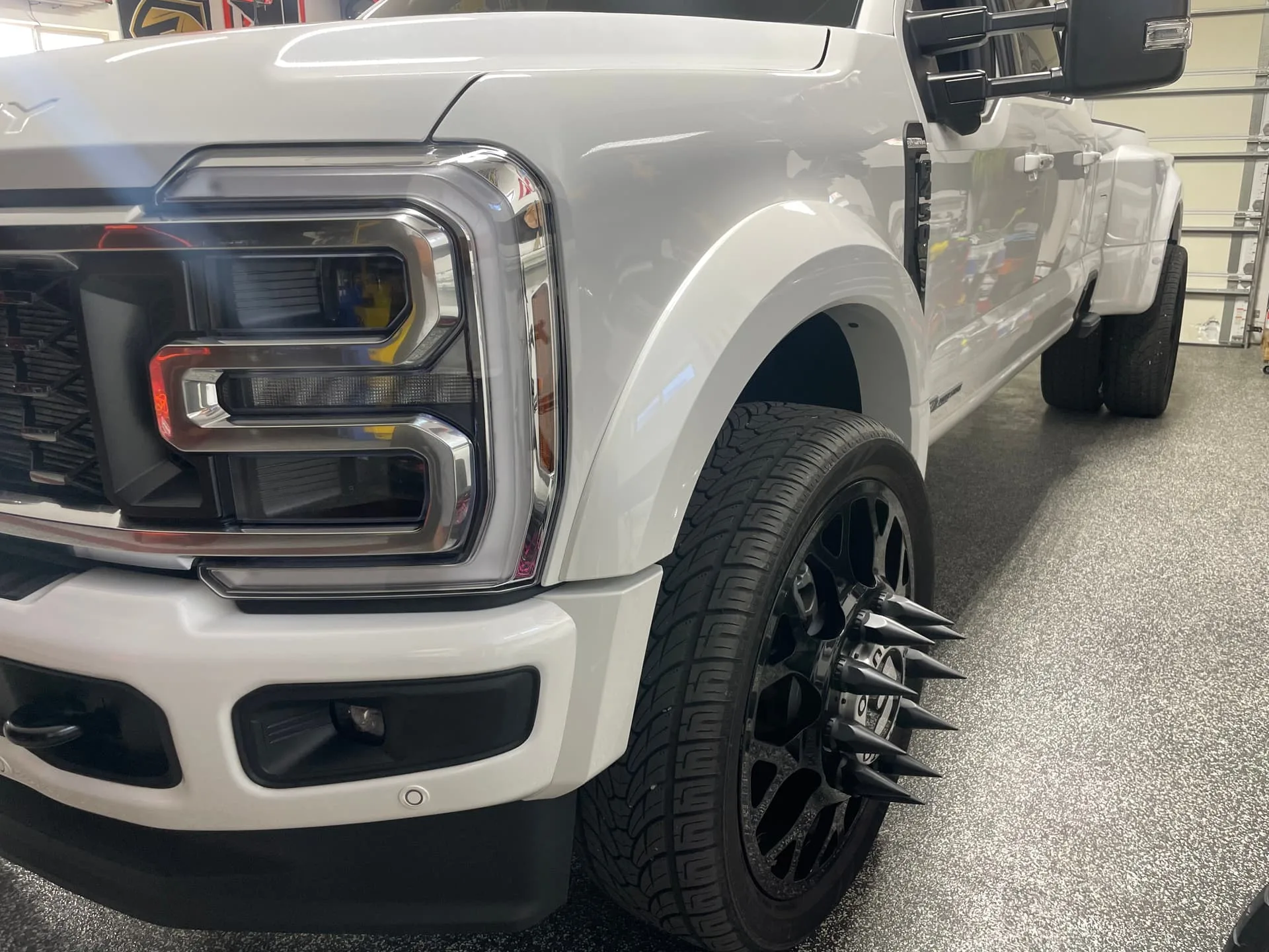 Close-up front driver-side Robert's white Ford F450 dually with spiked lug nut covers and LED headlights photo 2