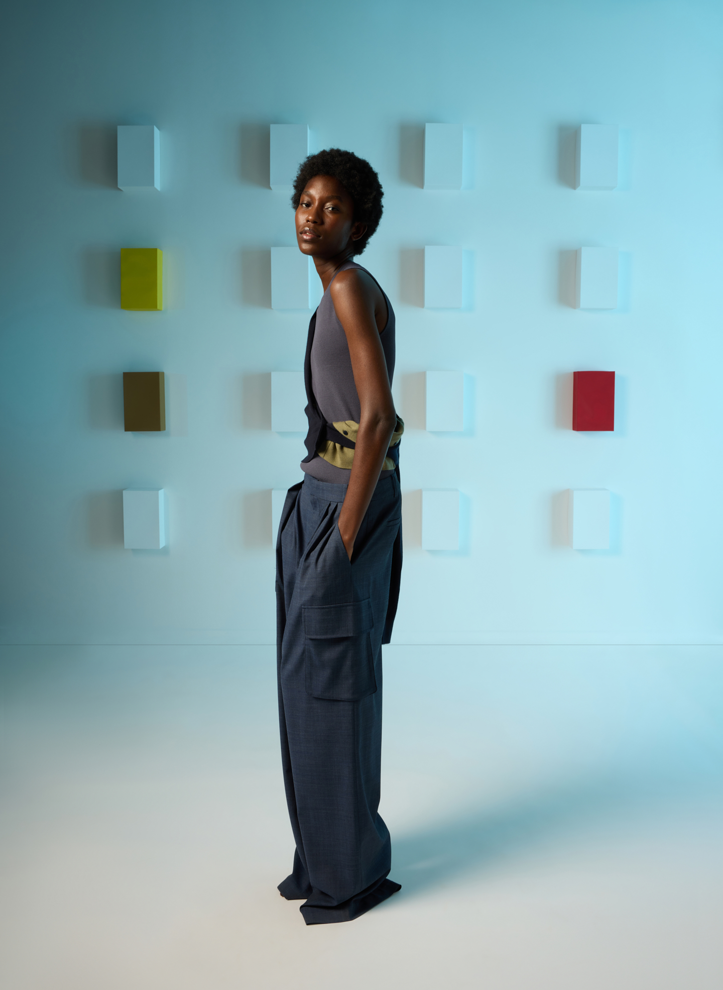 A person in stylish clothing stands against a colorful abstract background.