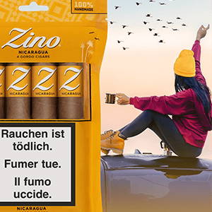 Ein Freshpack mit Zino Nicaragua Gordo-Zigarren vor einem Hintergrund mit einer jungen Frau, die ein heisses Getränk auf dem Dach ihres Auto trinkt, während sie die Vögel am Horizont beobachtet.