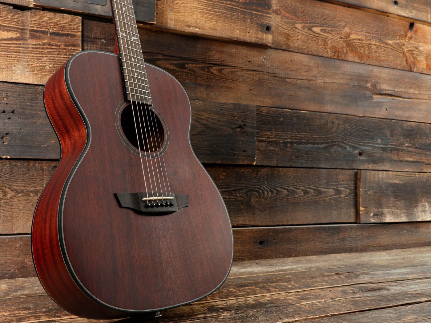 A brown acoustic guitar leaning against a wooden wall.