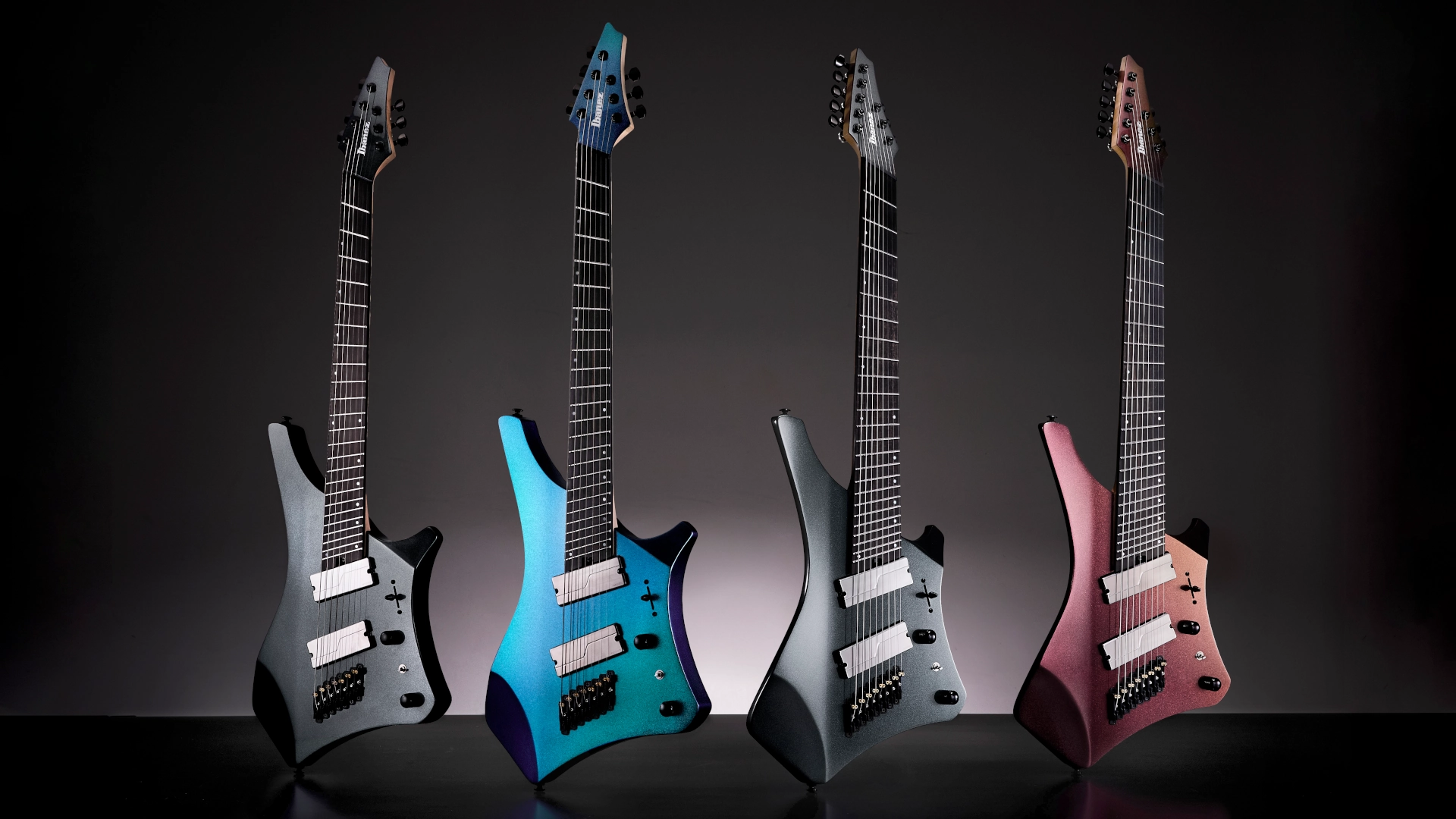 Four Ibanez Alpha Series guitars in various colours against a dark background.