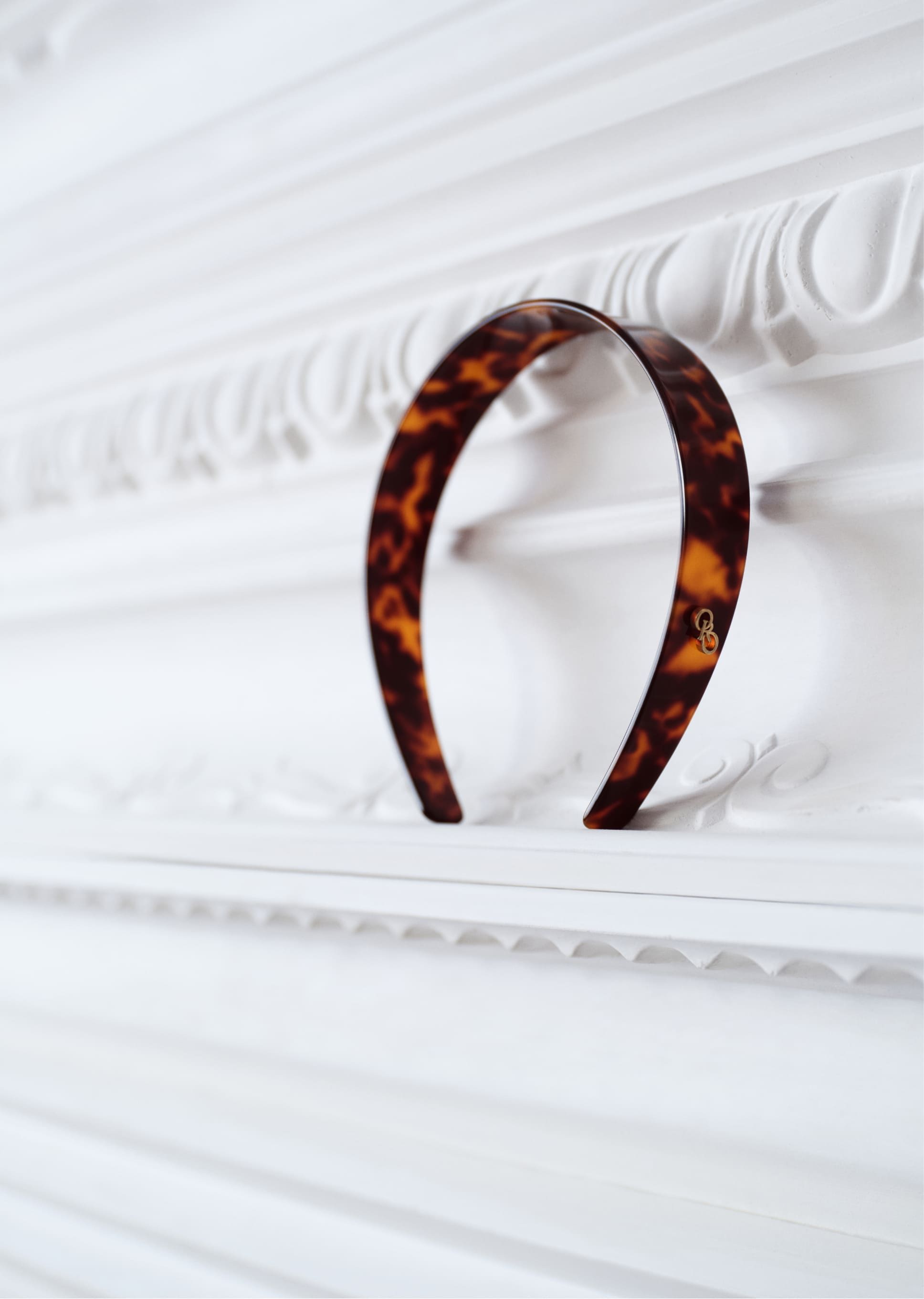 A tortoiseshell hairband resting on a white ornate surface.