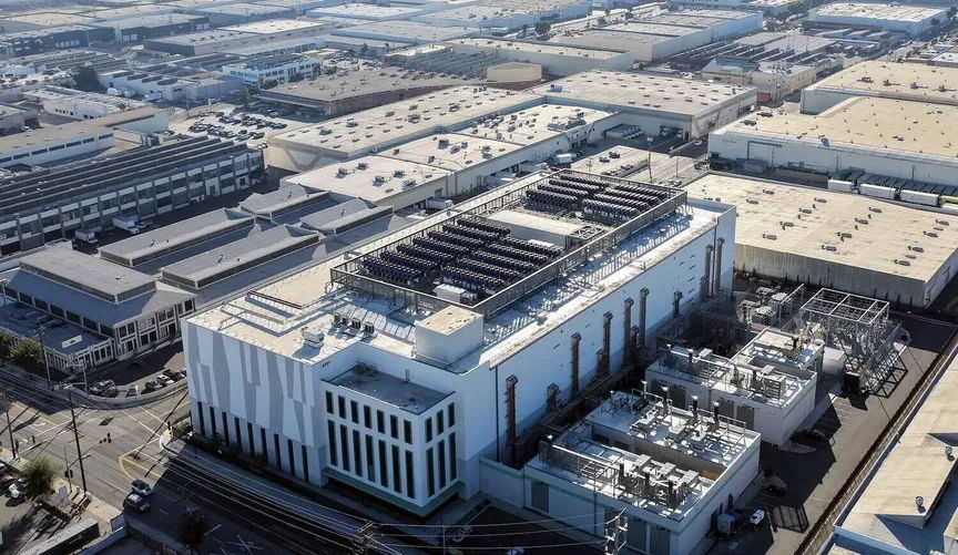 Aerial view of a modern building with solar panels surrounded by warehouses.