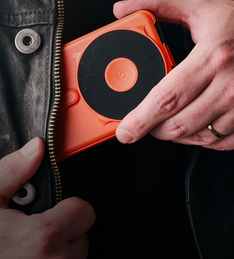 A person placing an orange device into a jacket pocket.