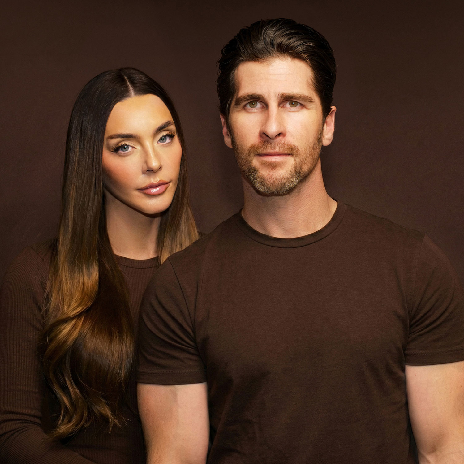 A woman and a man posing together against a dark background.