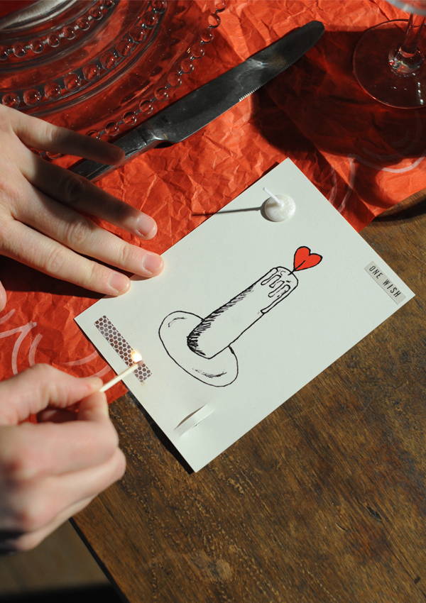 A hand striking the match on a Love Candle Wish Card.