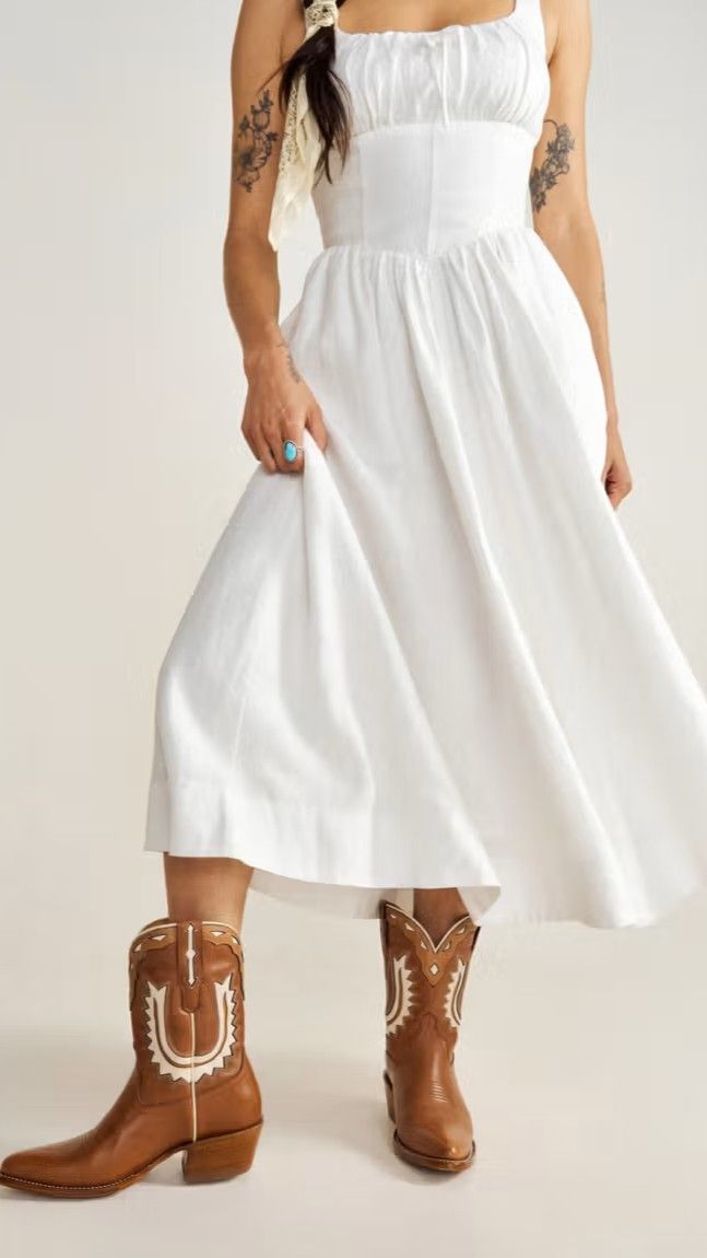Woman wearing a white dress and brown cowboy boots.