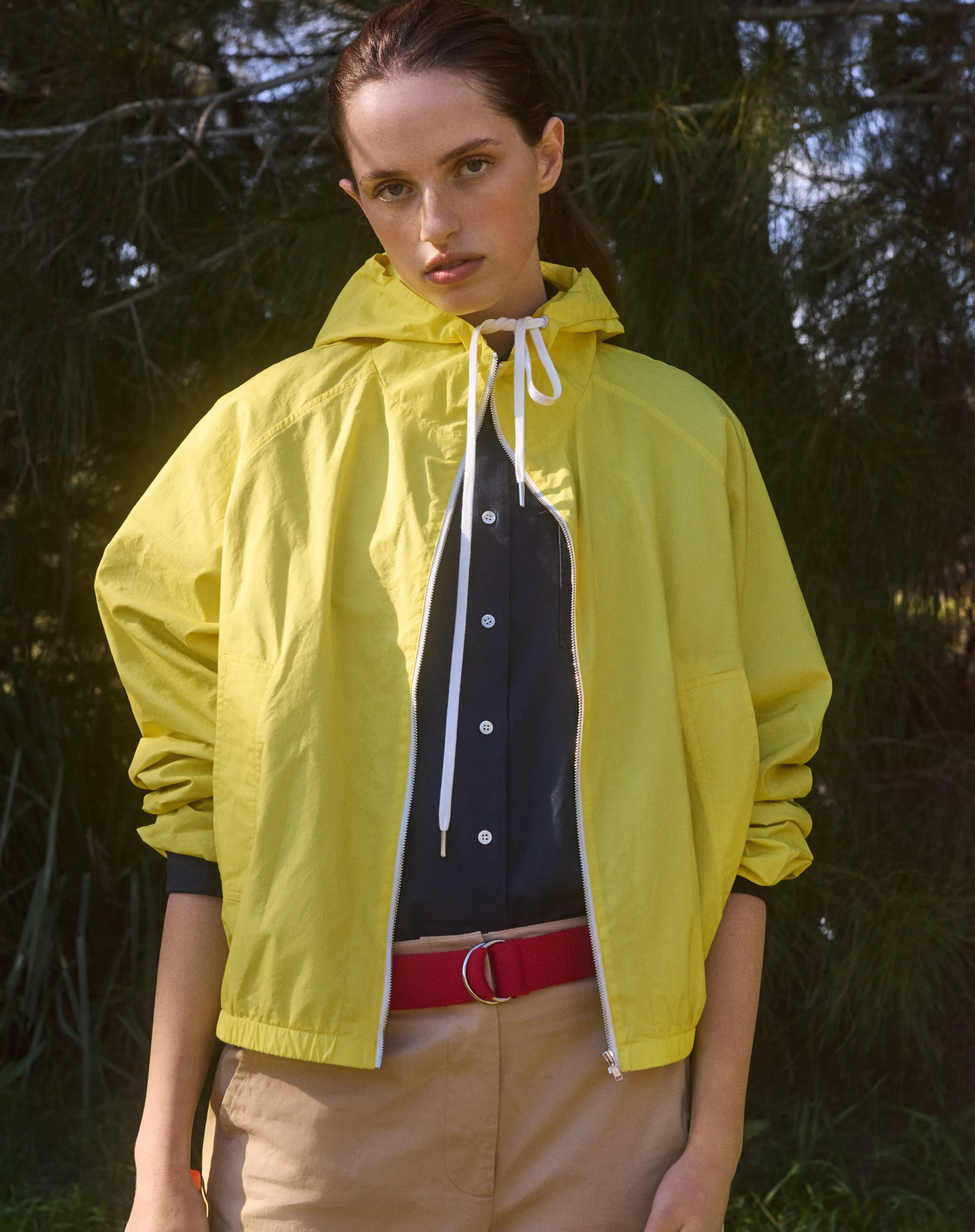 A model in a yellow jacket with a belt, posing outdoors.