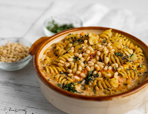 Bowl of creamy pasta topped with pine nuts and herbs.
