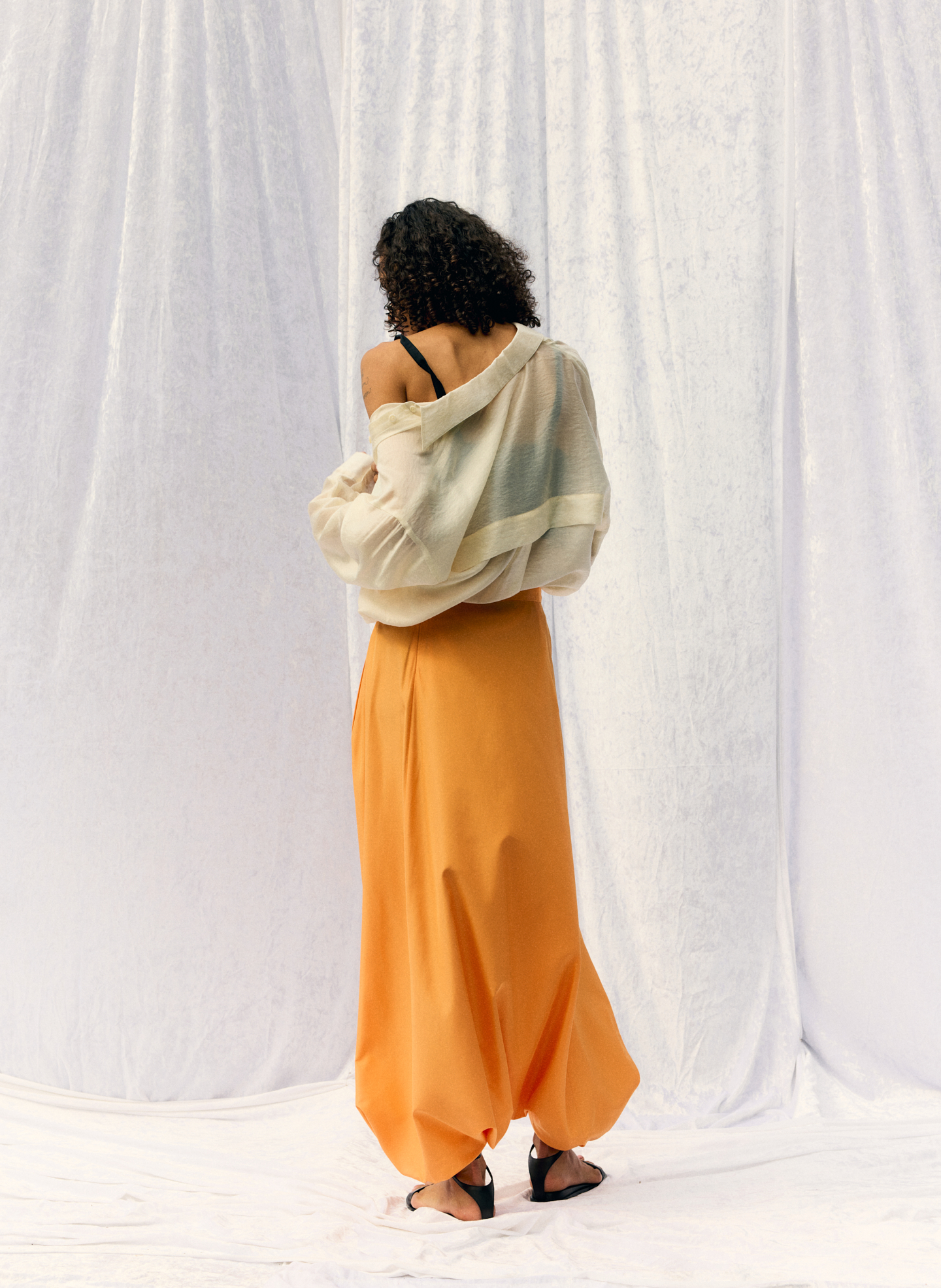 Woman in orange skirt and light sweater, facing away from the camera.