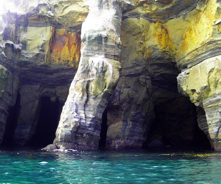 A photo of two sea caves on the cliffside, with the ocean right beneath them.