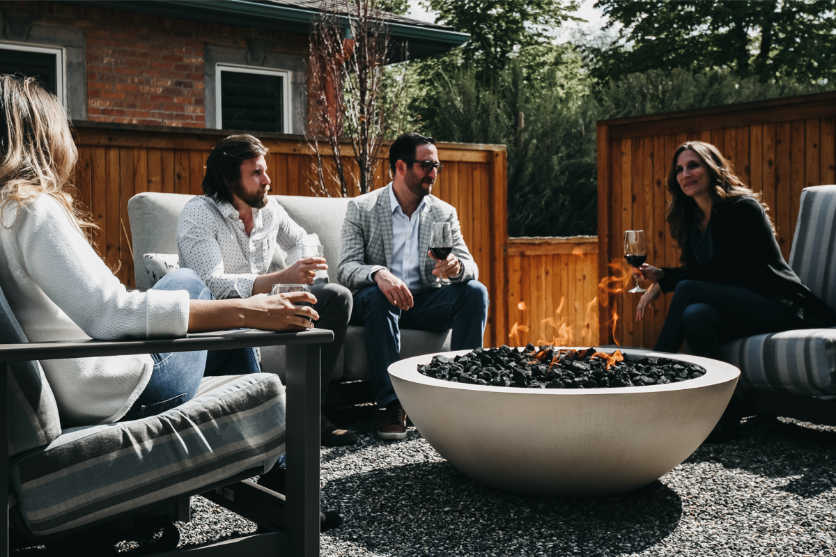 Guests seated around a round outdoor fire pit, creating a casual fire pit seating area for backyard entertaining. 