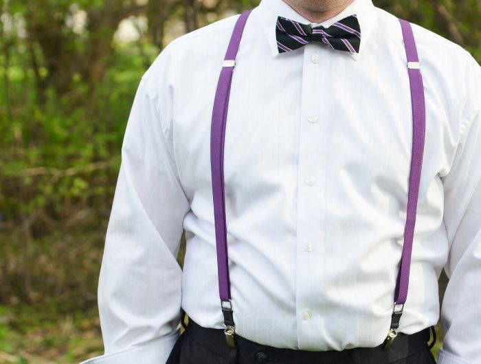 Groomsman wearing purple skinny suspenders and a coordinating black and purple striped bow tie
