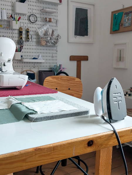wool pressing mat for quilting on a desk next to a sewing machine and a mini iron with a quilt block
