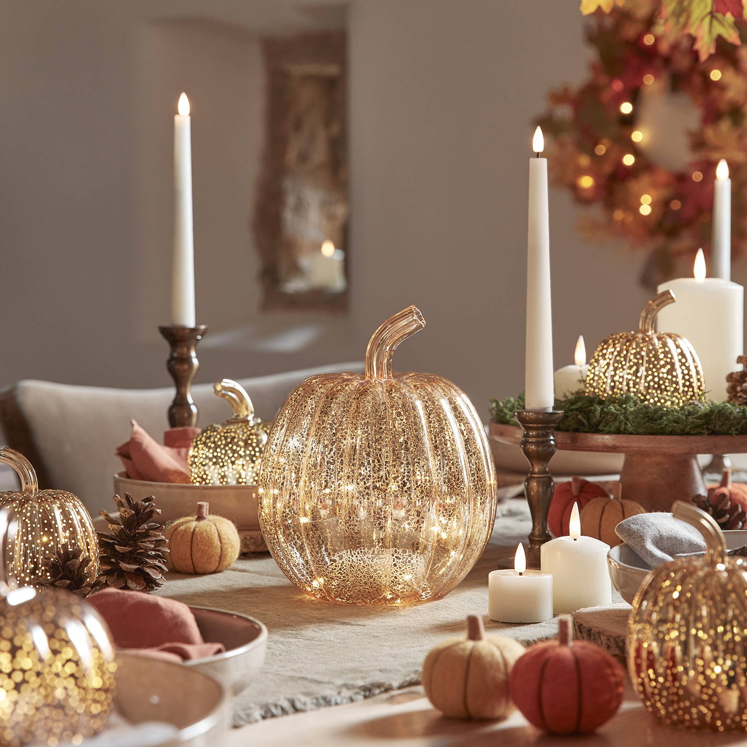 A gold mercury pumpkin as part of an autumnal dining display with LED candles.