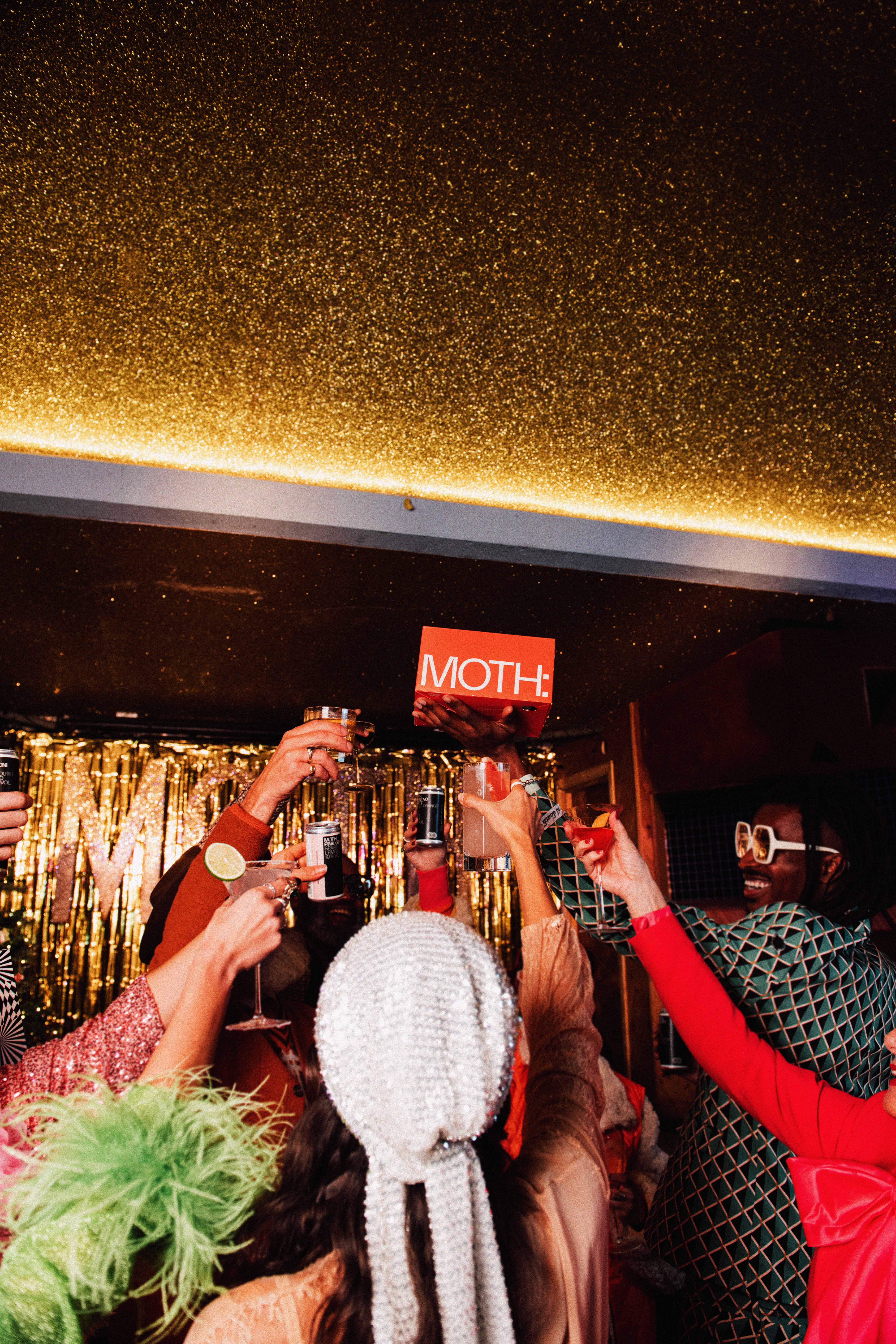 People celebrating with drinks, holding a sign that says 
