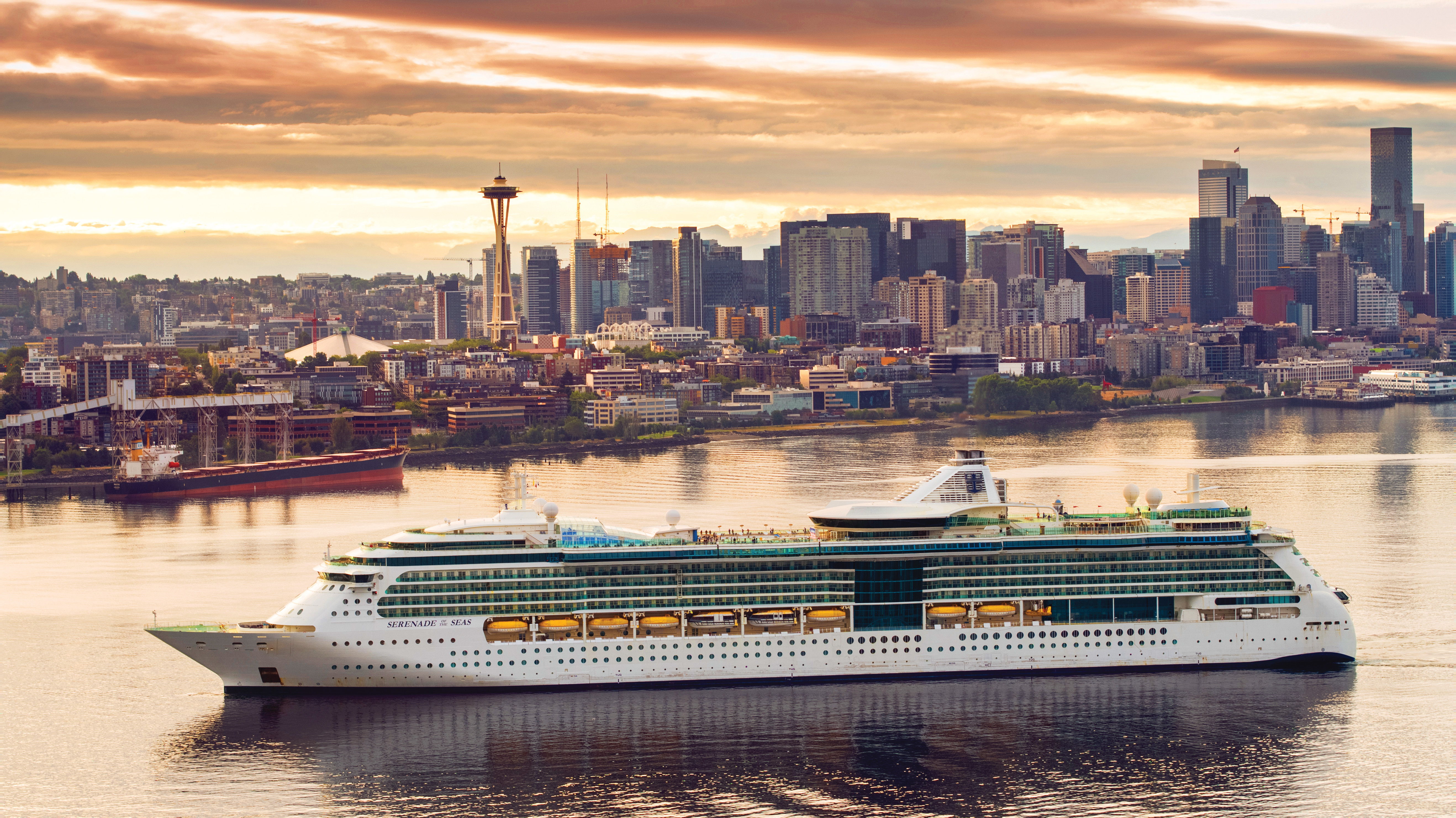 Cruise ship sailing near a city skyline during sunset.