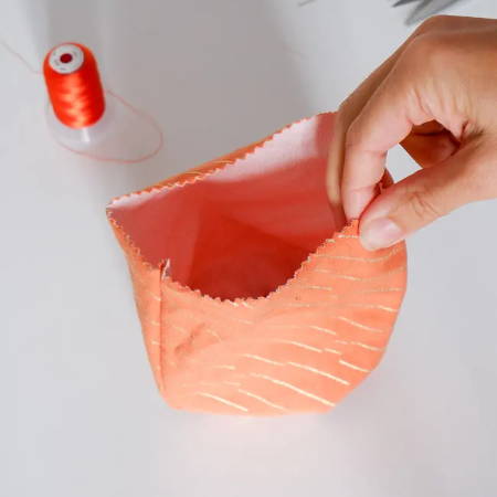 Hand holding an orange fabric bowl that will be stuffed, right side out