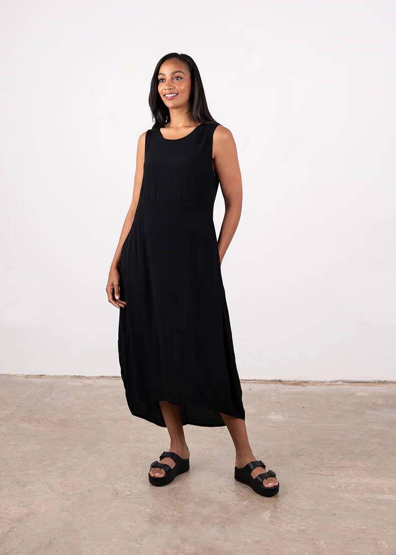A model wearing an oversized, black, cocoon style sleeveless dress with chunky black platform slides