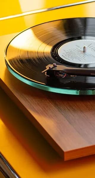 A vinyl record player on a wooden surface with a yellow background.