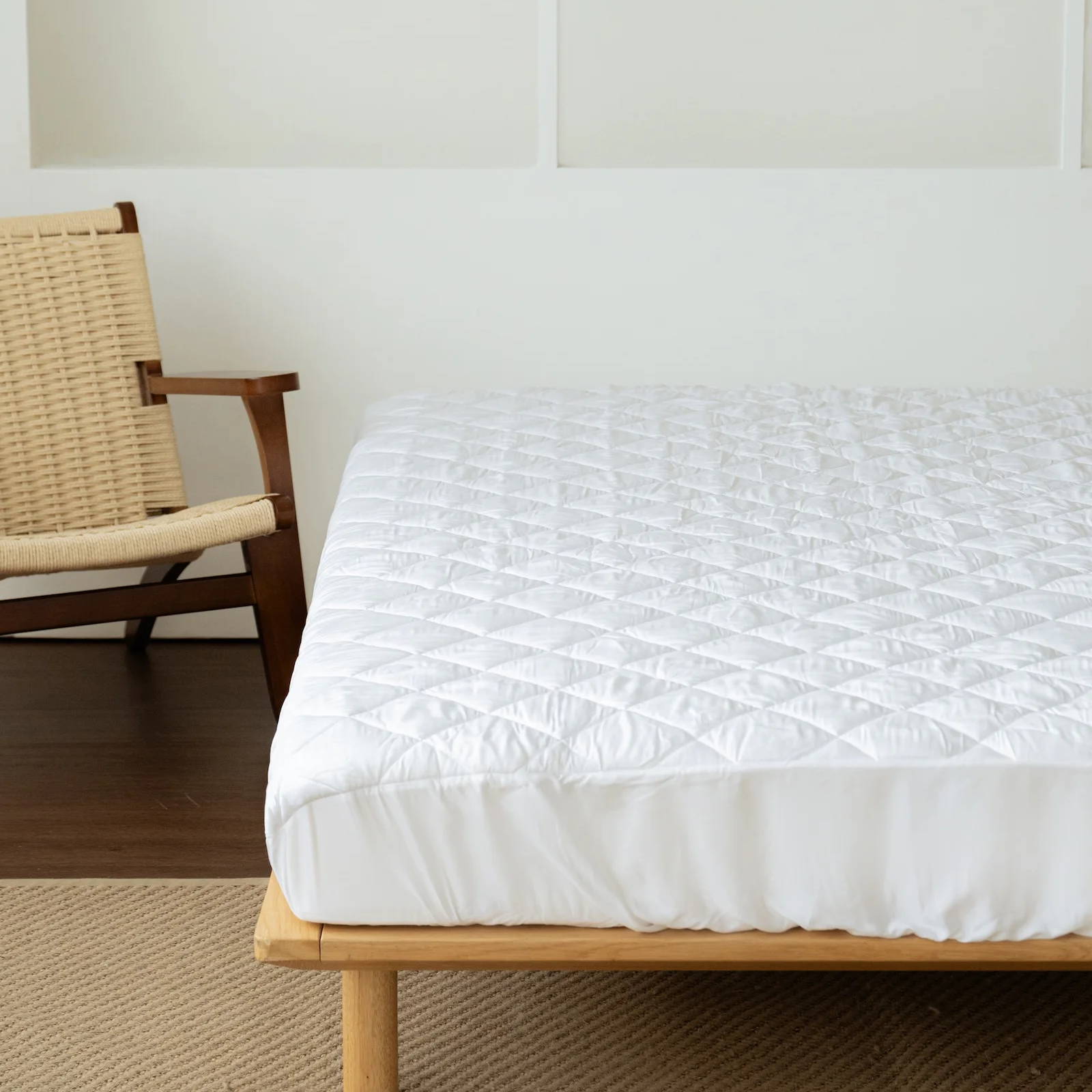 a white mattress protector tucked neatly over a mattress on a wooden bed frame