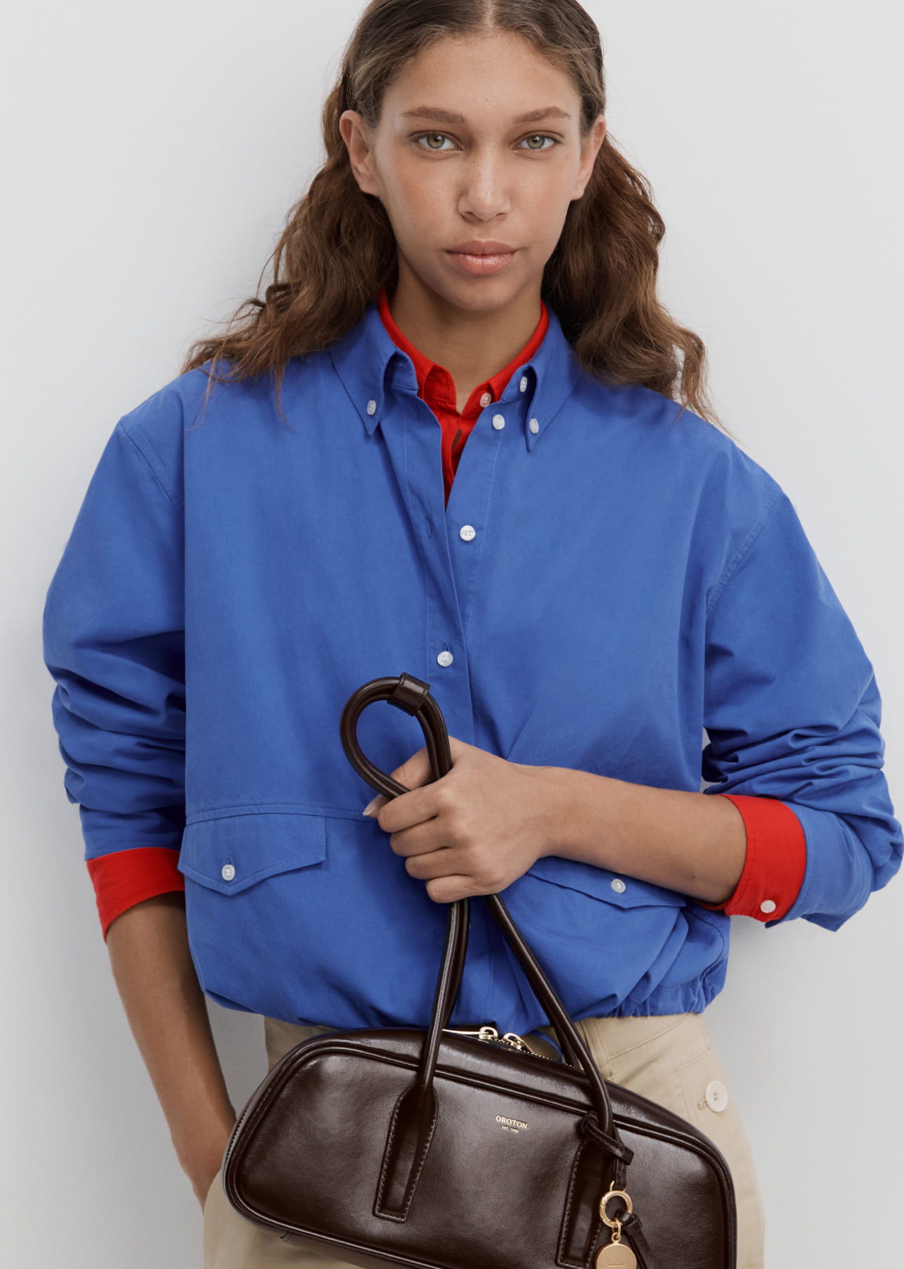 Young woman in blue shirt holding a brown handbag.