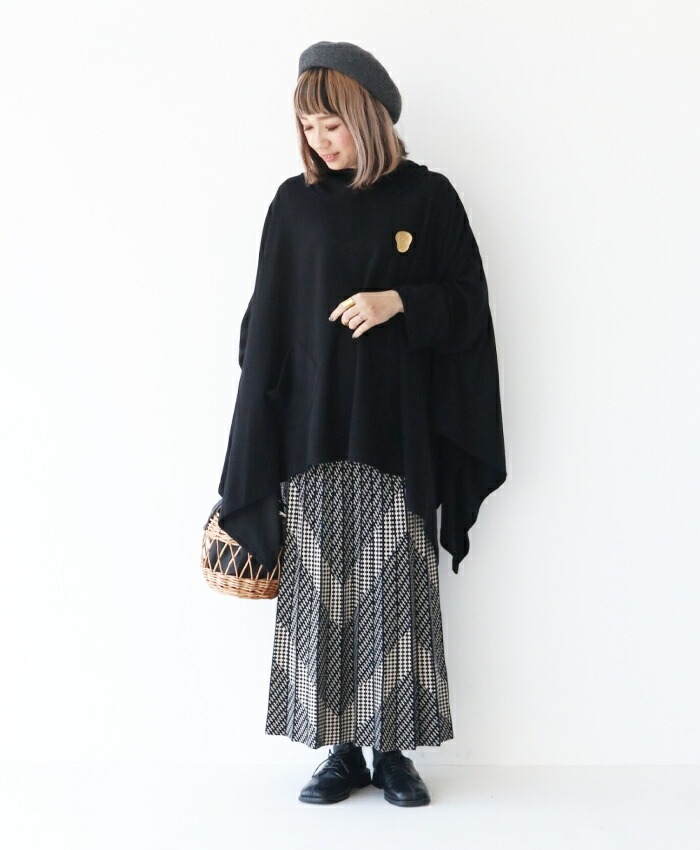 Person wearing a black poncho, patterned skirt, and beret, holding a basket.