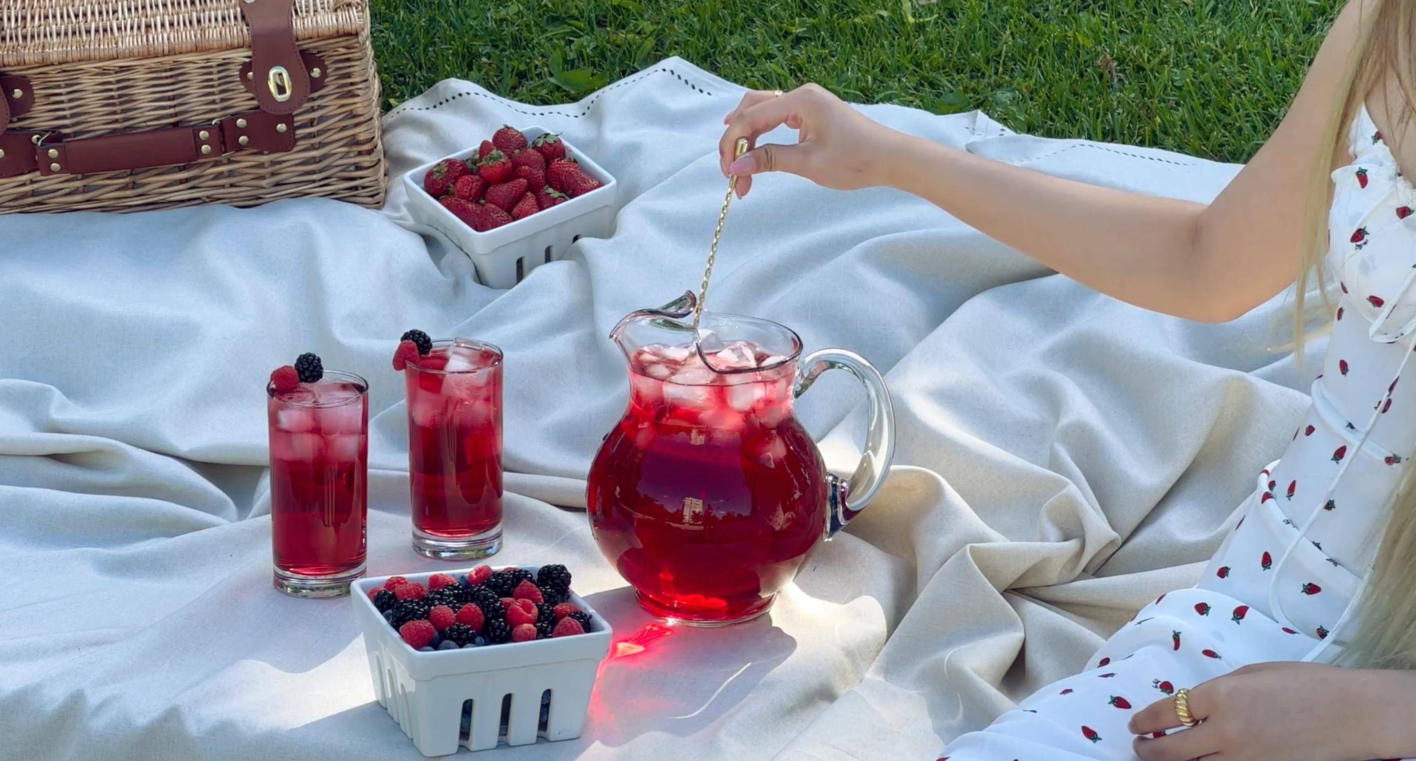 Picnic with girl stirring tea leaves berry iced tea in pitcher and two glasses  