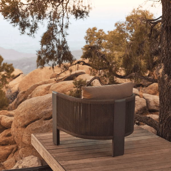 Curved outdoor lounge chair with woven rope back and weather-resistant cushion overlooking a rocky desert landscape