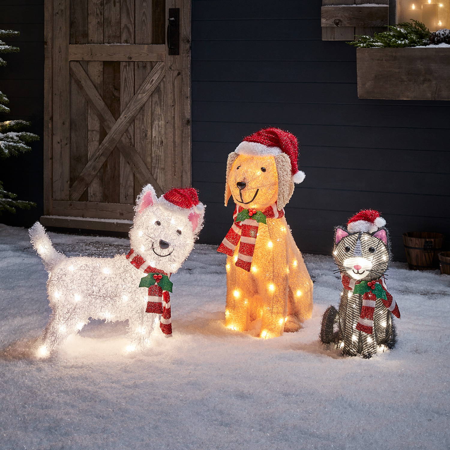 Cat, Scotty dog and Labrador figures wearing Santa hats in a snowy setting 