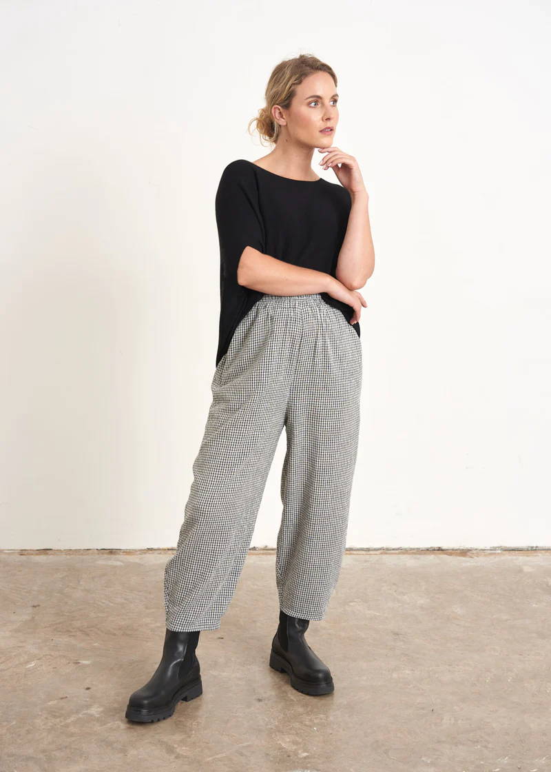 A model wearing a pair of grey and white check barrel leg trousers with a black top and black chunky chelsea boots
