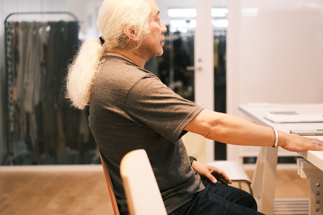 Person sitting at a table, profile view, with long white hair.
