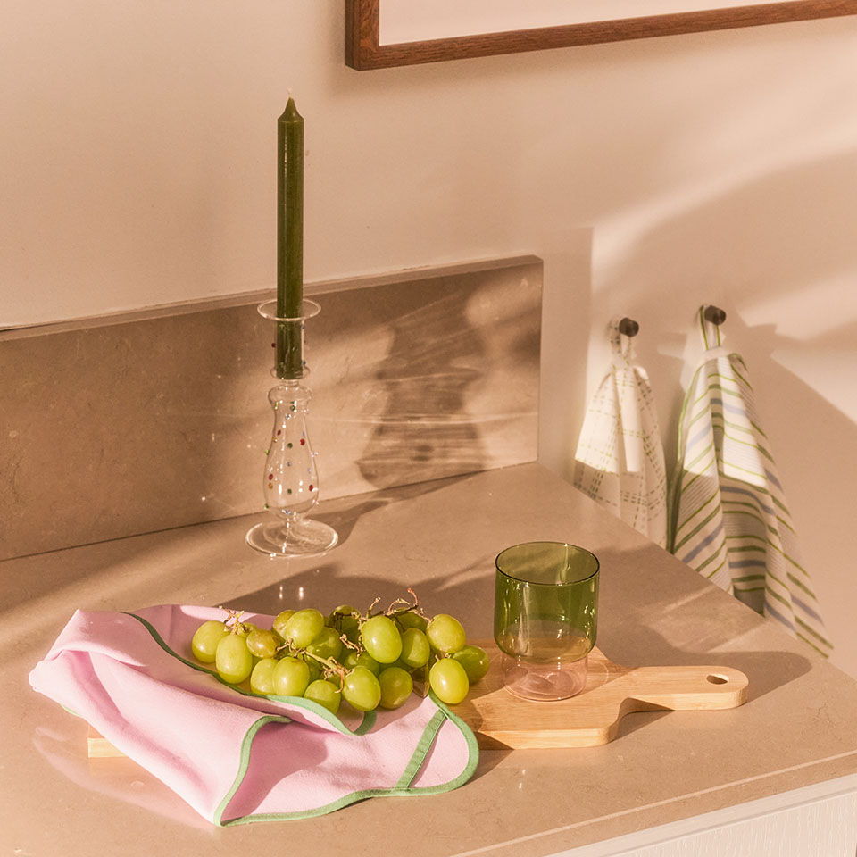 A countertop with grapes, a candle, and kitchen towels.
