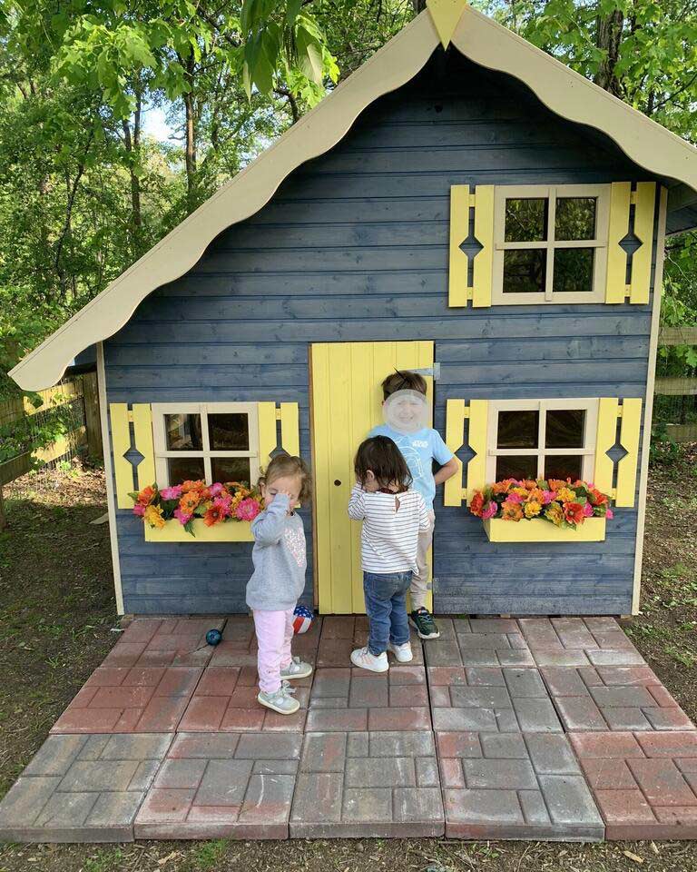 Kids Playhouse in gray color with yellow door and window shutters with kids on the terrace in a backyard by WholeWoodPlayhouses