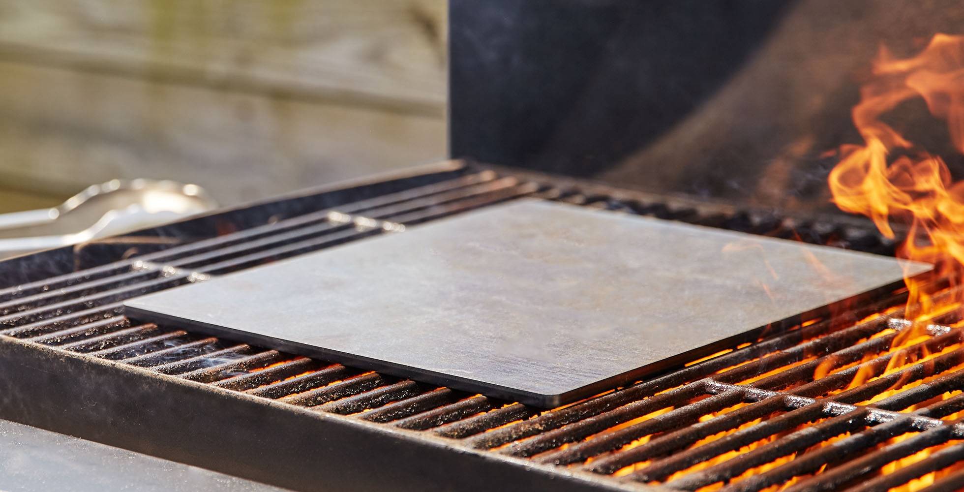 An empty Misen Oven Steel sits on an outdoor grill, with open flame visible in the foreground.